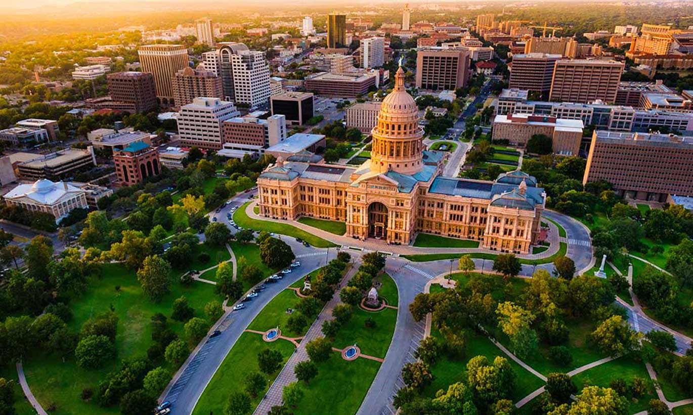 An aerial shot of the Texas Capitol building and lawn in Austin, Texas at sunset