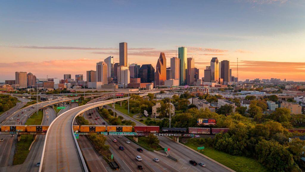 Trains and cars intersect across roadways and railways with downtown Houston in the background