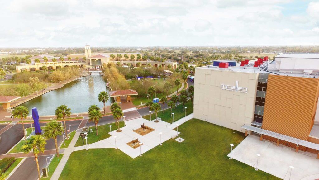 The McAllen Performing Arts Center is next to a large pool of water and many palm trees.