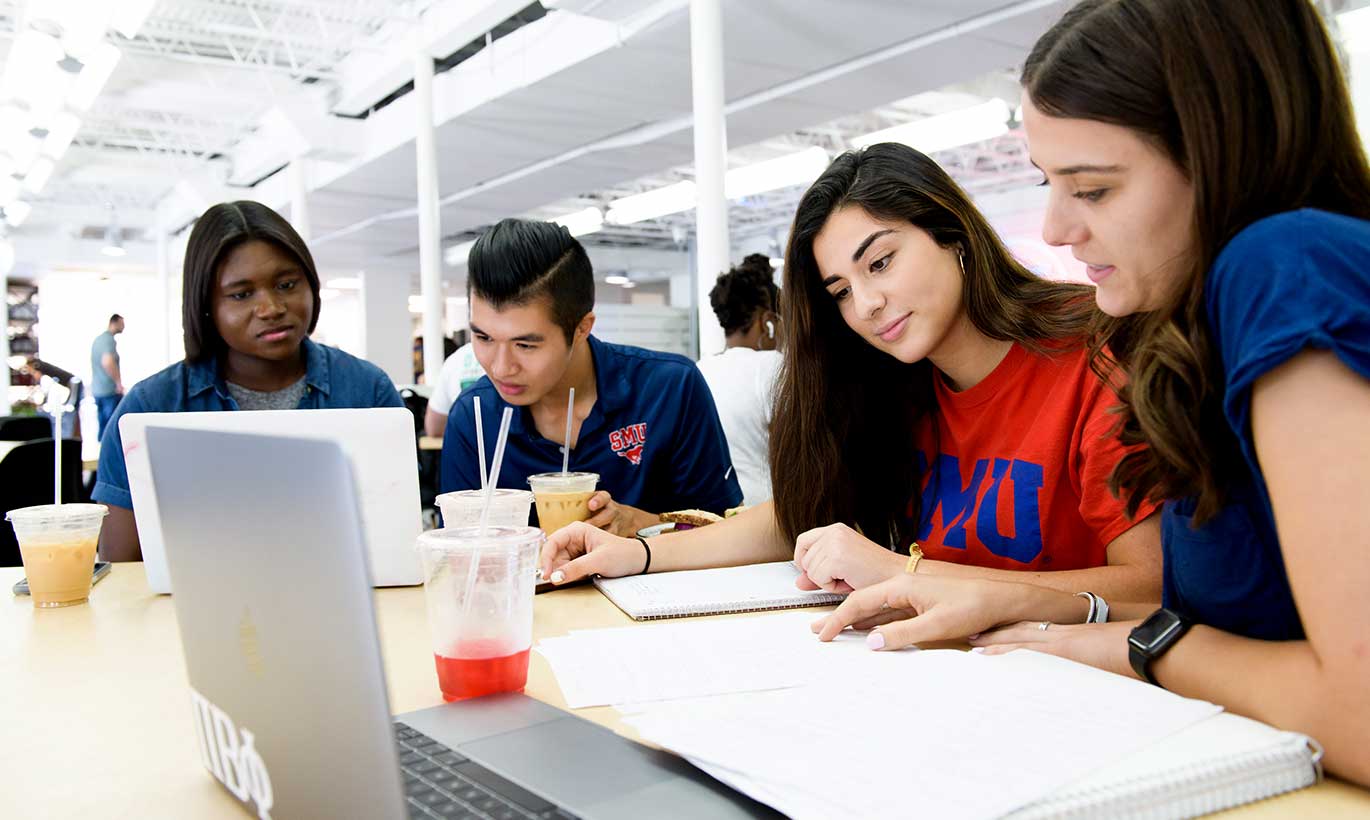 Four students at Southern Methodist University sit at a table, studying on their laptops.
