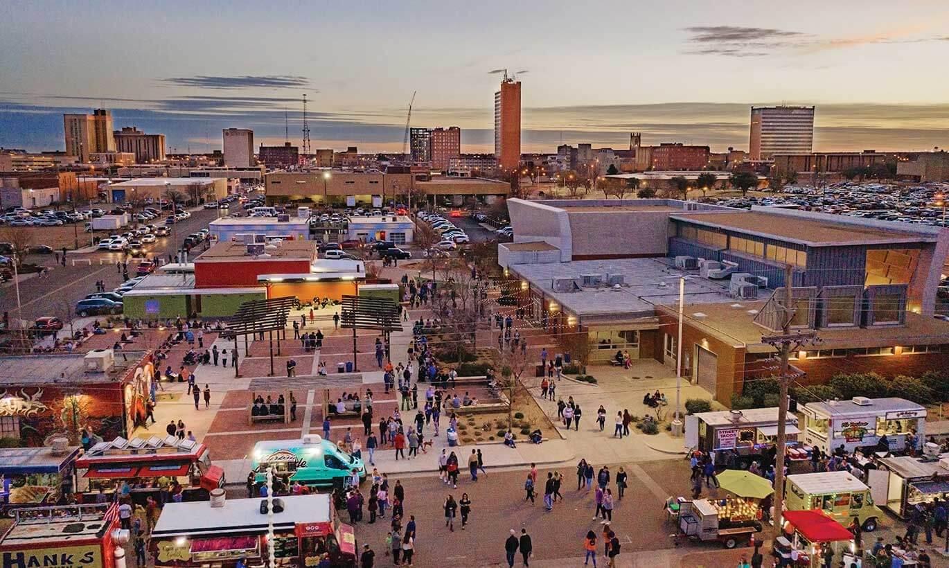 Residents of Lubbock, Texas stroll through the First Friday fair with food trucks in a central town plaza area.