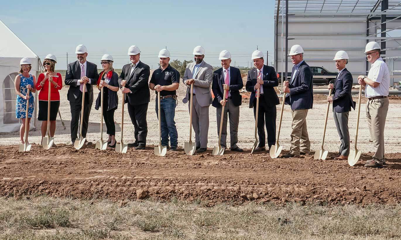 Men and women wearing hard hats and business clothing holding shovels at a groundbreaking event