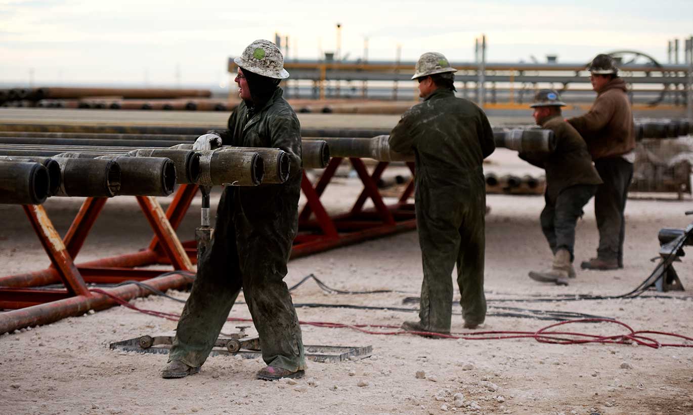 Workers handle large metal equipment at an oil facility in Midland, Texas
