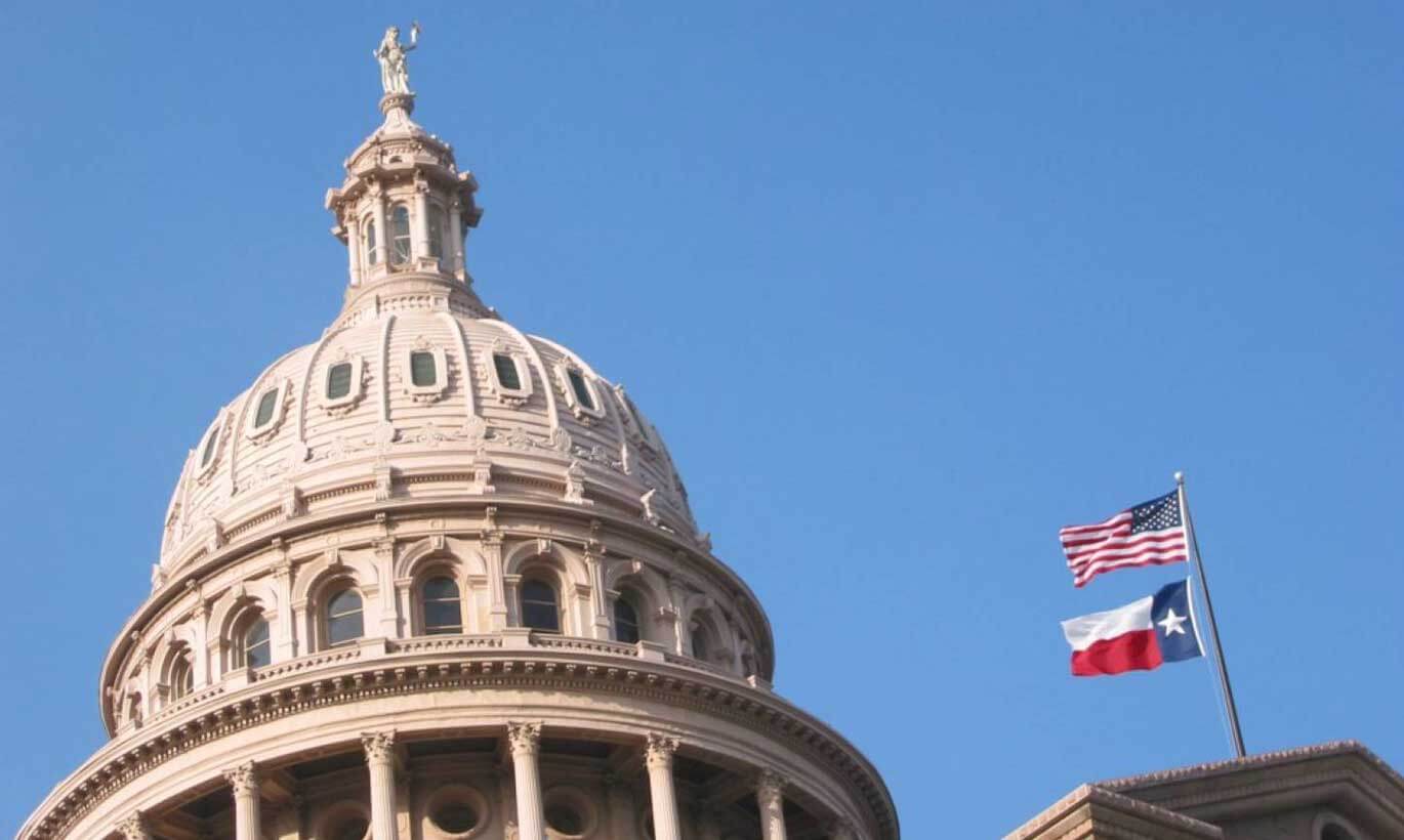 The dome of the Texas Capitol building with the U.S. and Texas flags flying in Austin, Texas