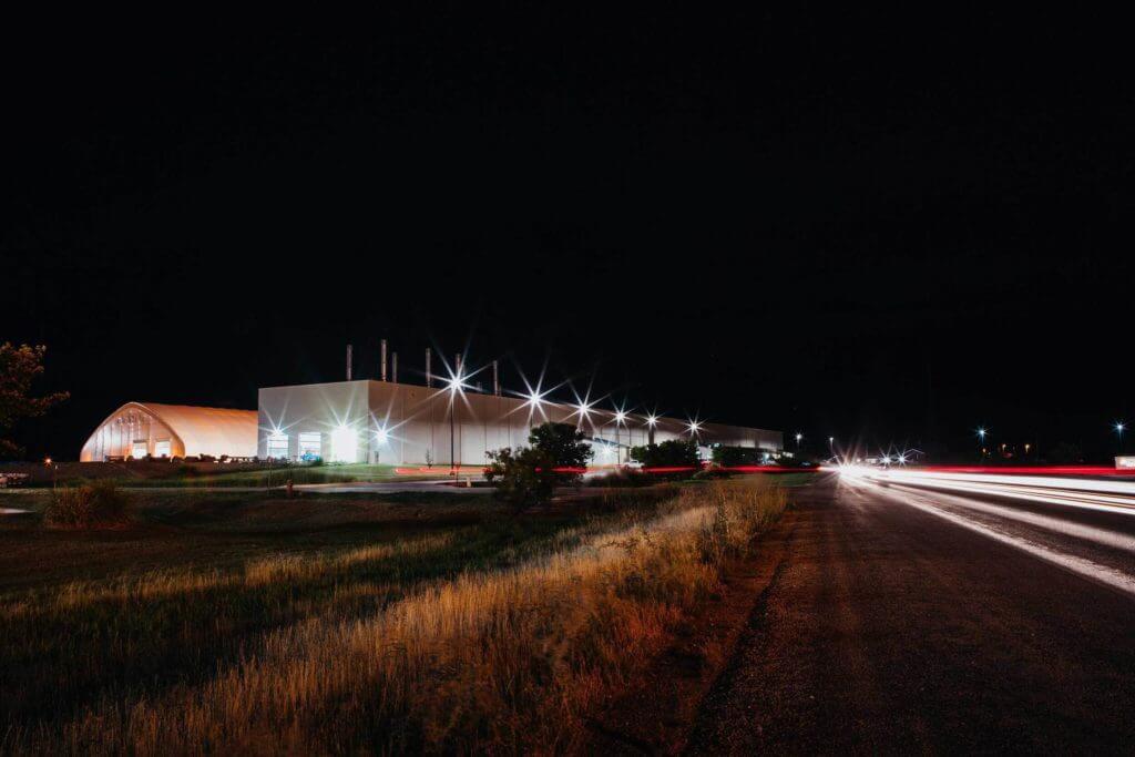 Cars on a highway drive past a large industrial facility lit up at night in Abilene, Texas.