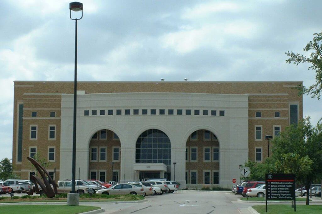 A large white and brown campus building at Texas Tech University sits in front of a parking lot filled with many cars.