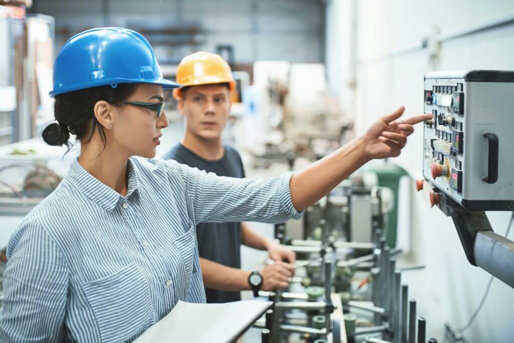 A woman in a blue hard hat flips on a switch in a manufacturing facility.