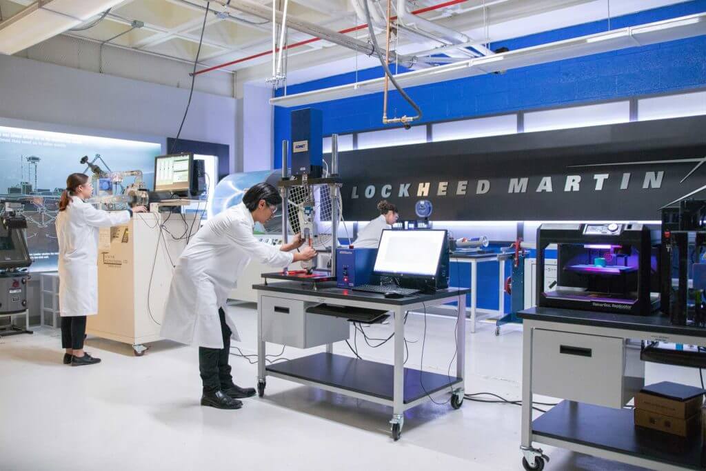 Three workers work with industrial machinery and computer equipment at Lockheed Martin