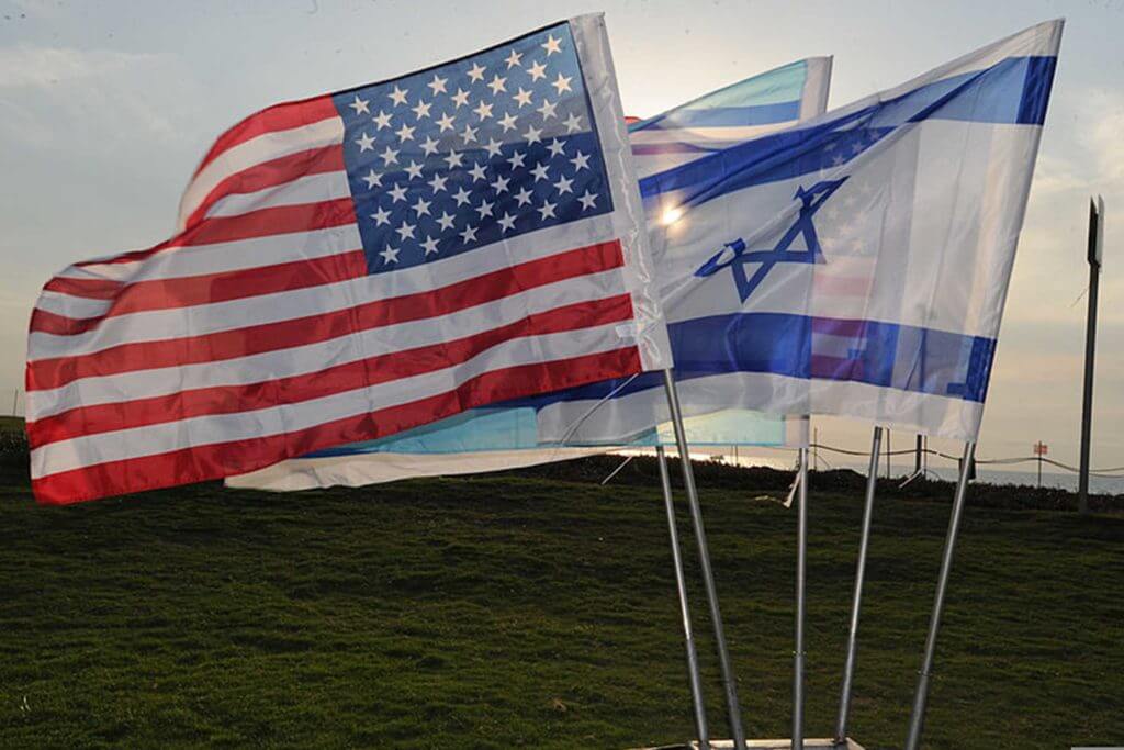 The Israel flag and American flag are flown side-by-side in a field.