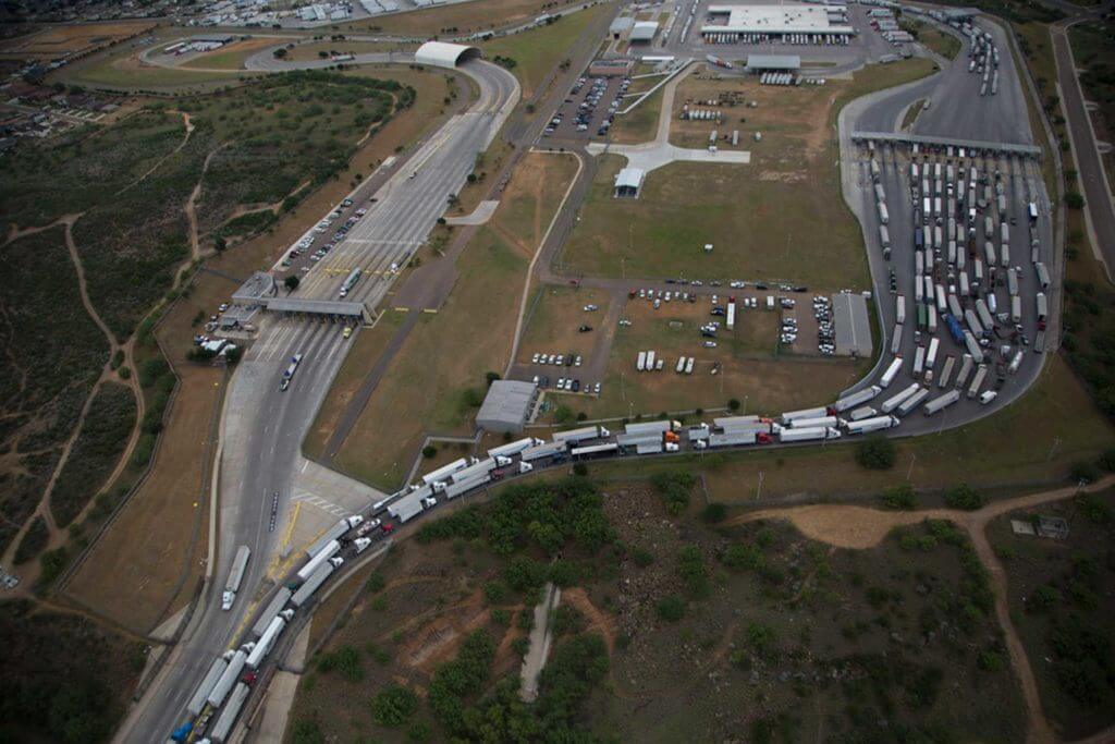 Hundreds of trucks lined up on a road pass through a trucking depot.