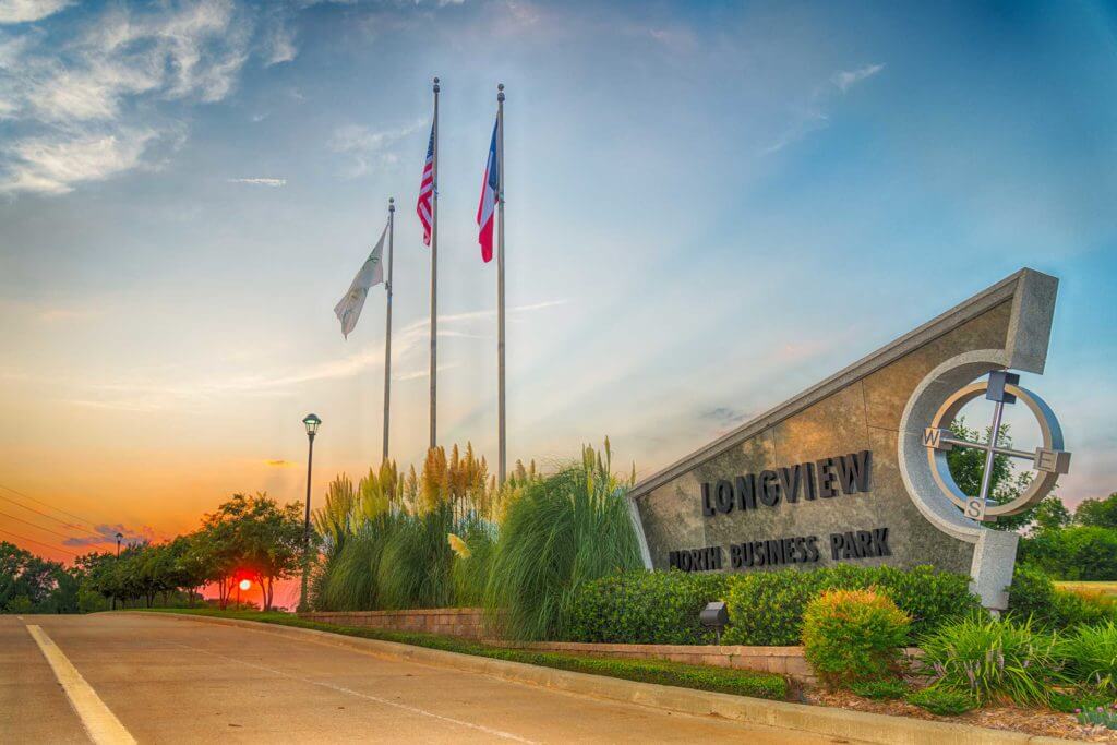 Three flags fly high next to a sign reading "Longview North Business Park" in Longview, Texas.