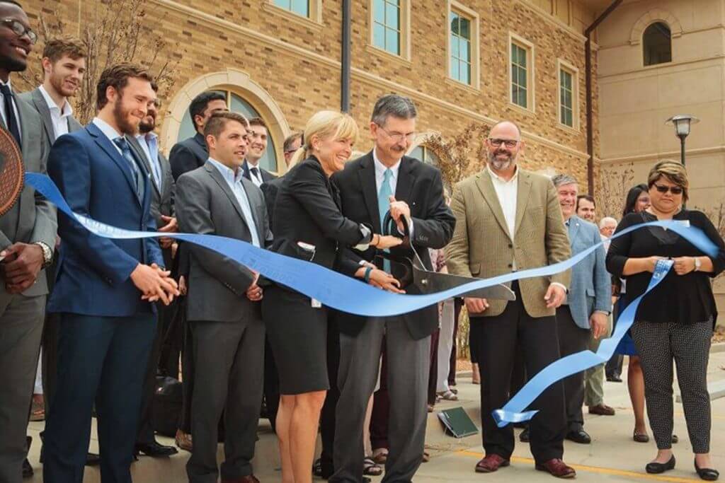 Men and women wearing business clothing cut a large blue ribbon at a ceremony to open Texas Tech Innovation Hub.