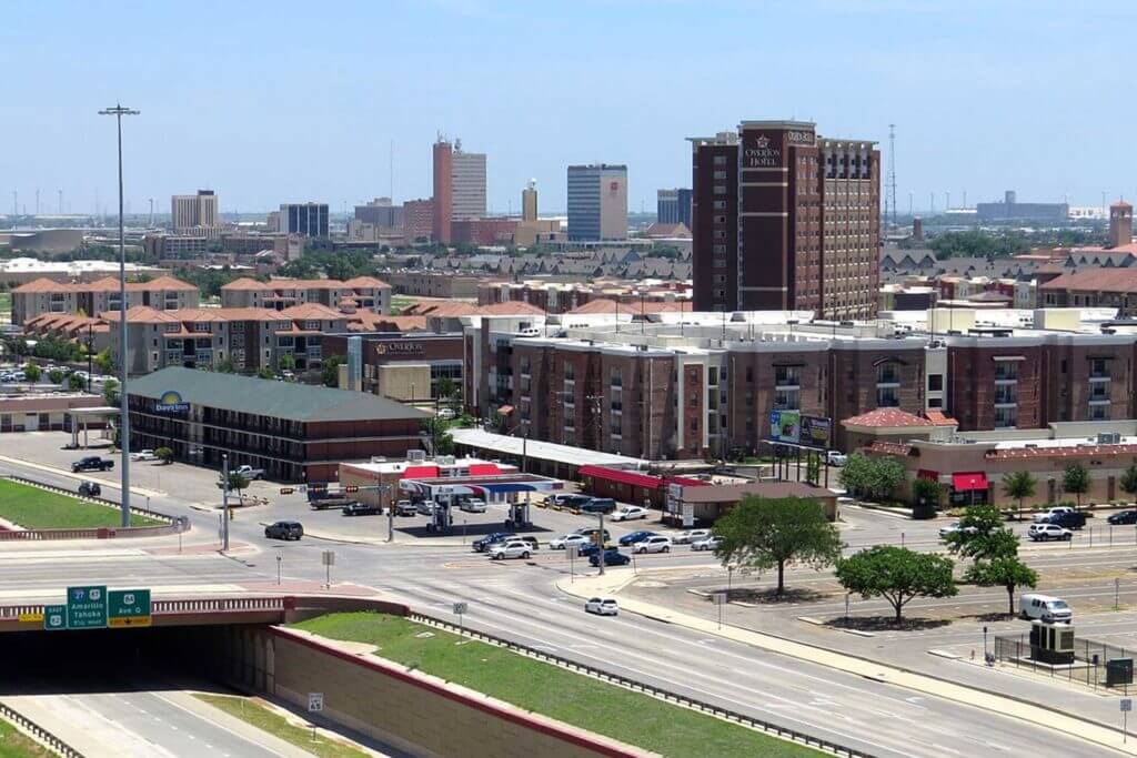 Cars drive through downtown Lubbock next to hotels and office buildings.