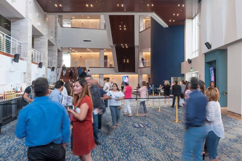 People walk through a tall building with high ceilings and blue and white light fixtures.