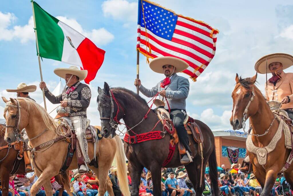 Men mount horses and carry the flags of Mexico and the US as they celebrate Charro Day