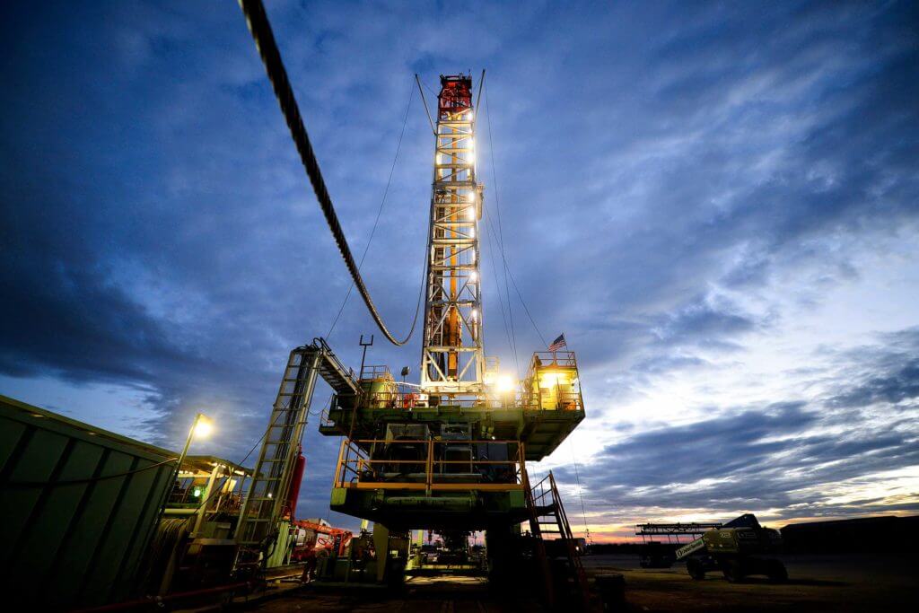 A large green oil rig surrounded by technical equipment is lit up at night in Midland, Texas.