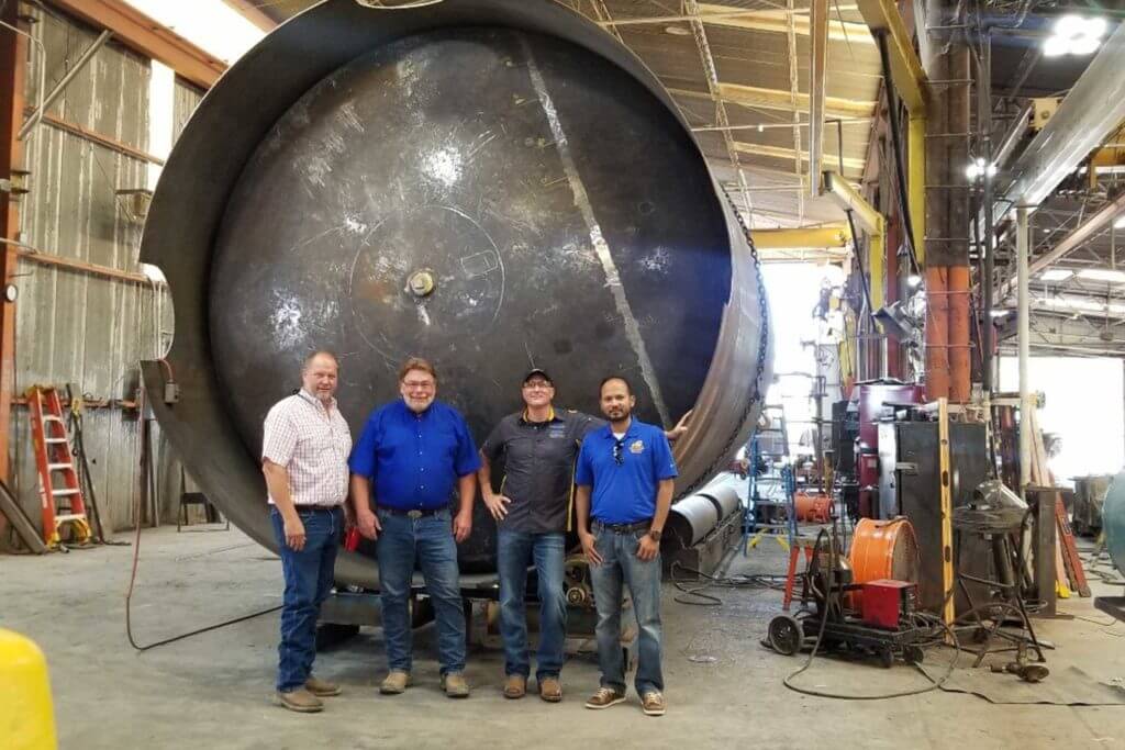 Four men stand in front of a huge metal drum at Wendland Manufacturing facility.