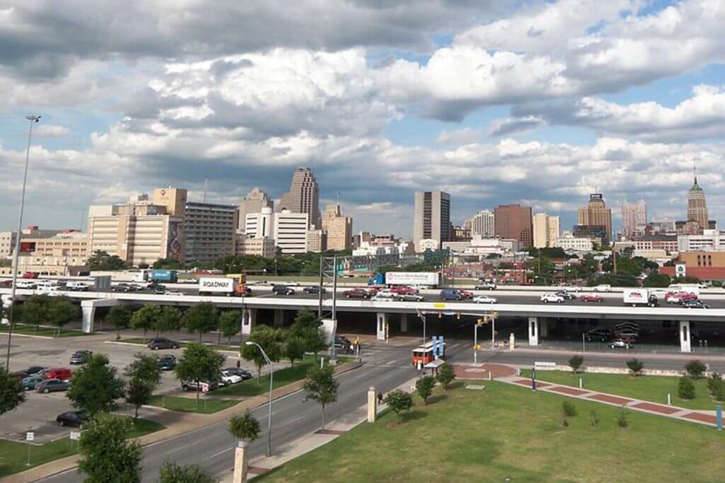 Highway of cars driving through downtown San Antonio, Texas with view of the city skyline behind it