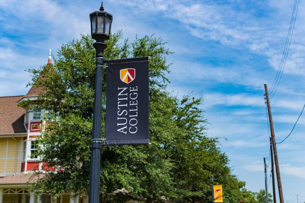 A banner on a lamppost reads "Austin College" with the school's red and yellow logo.