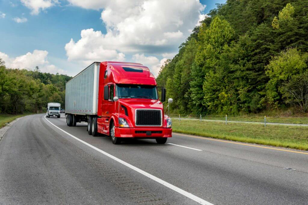 A large red truck drives down a major highway.