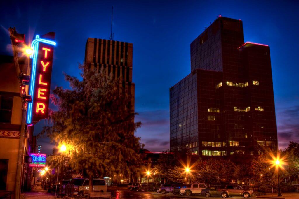 A neon sign that reads "Tyler" in red letters lights up downtown Tyler, Texas at night.