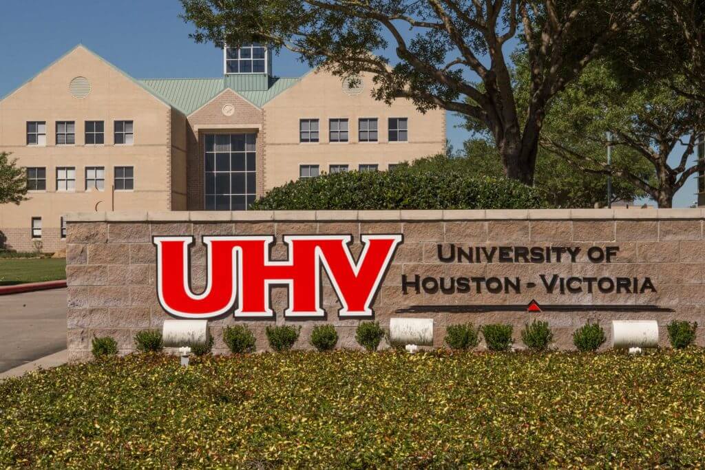 A brick sign reading "University of Houston Victoria" in front of a school building on campus