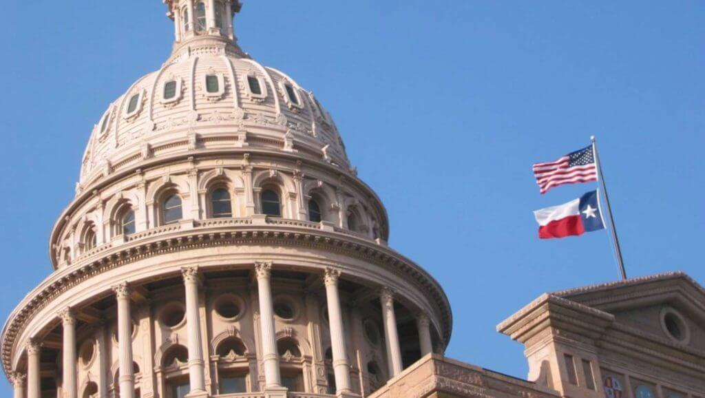 The dome of the Texas Capitol building with the United States and Texas flags flying in the sky in Austin, Texas.
