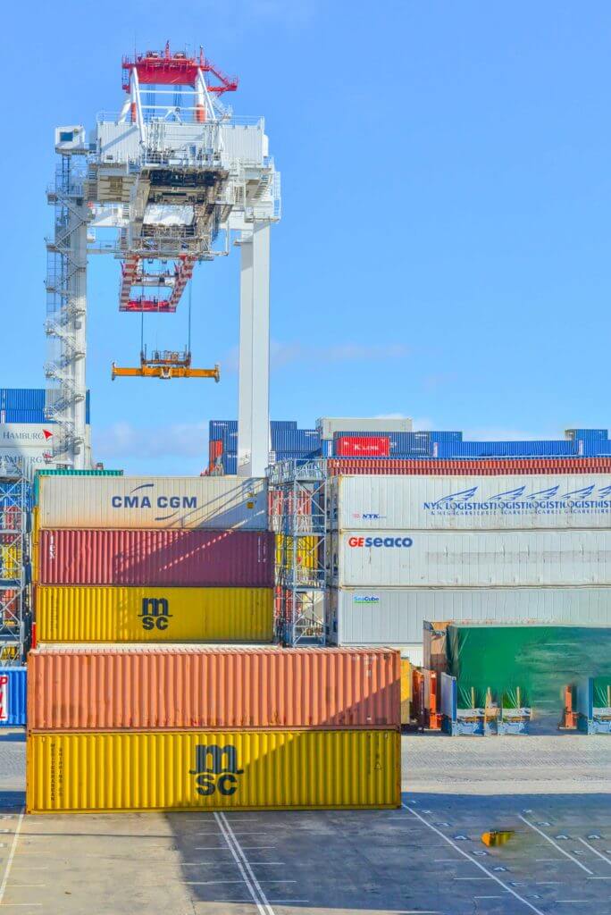 Multiple shipping cargo boxes are stacked on top of each other at a port.