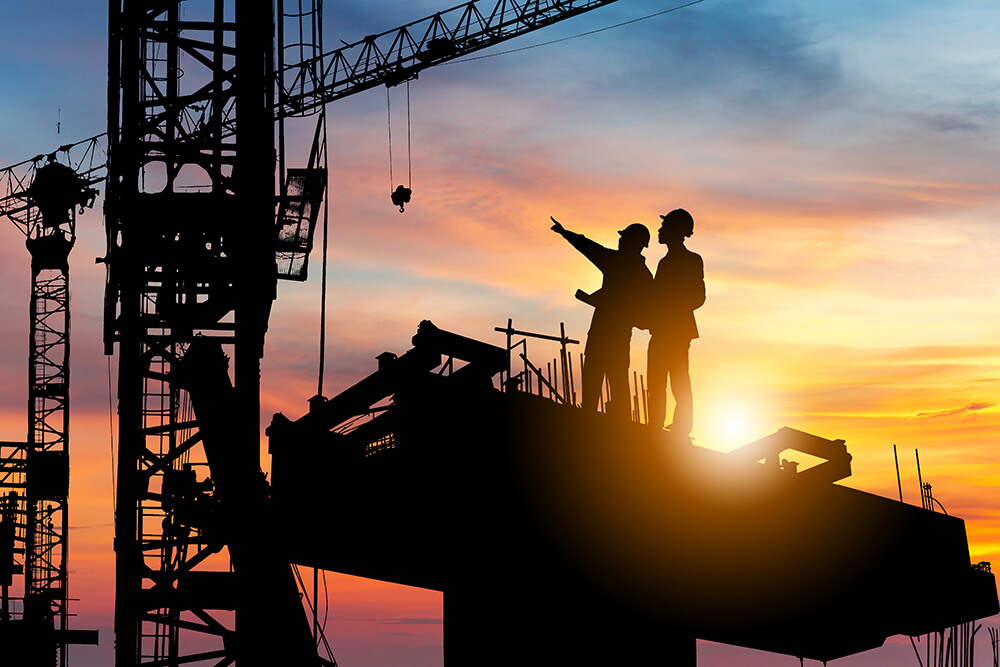 Construction workers stand on scaffolding at sunset