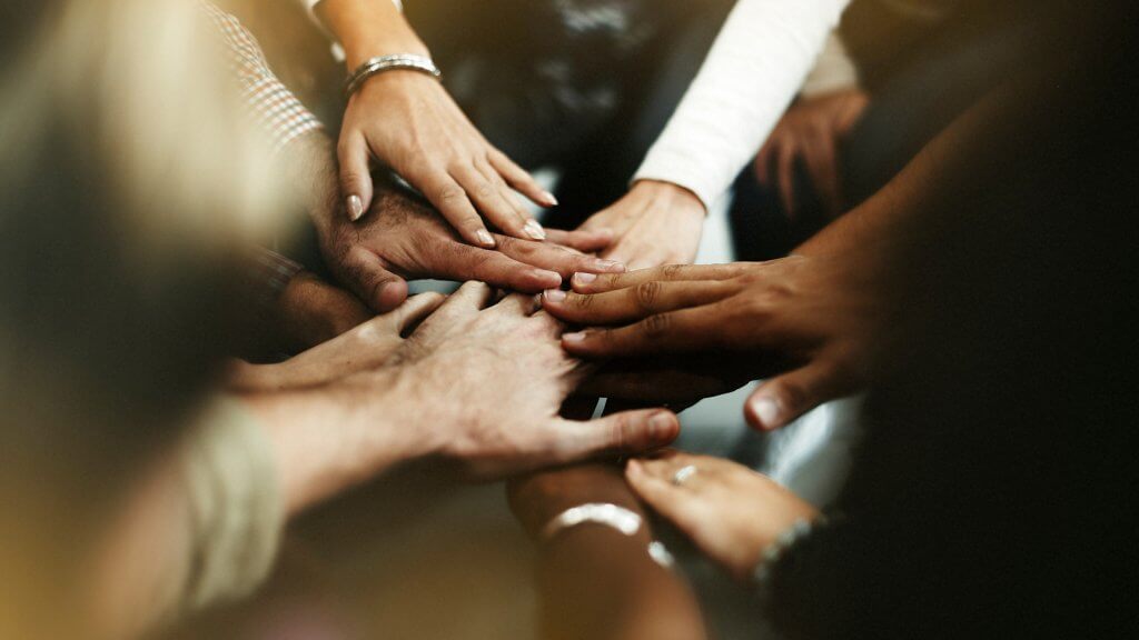 Hands stacked together in a gesture of unity and teamwork, symbolizing collaboration and shared commitment.