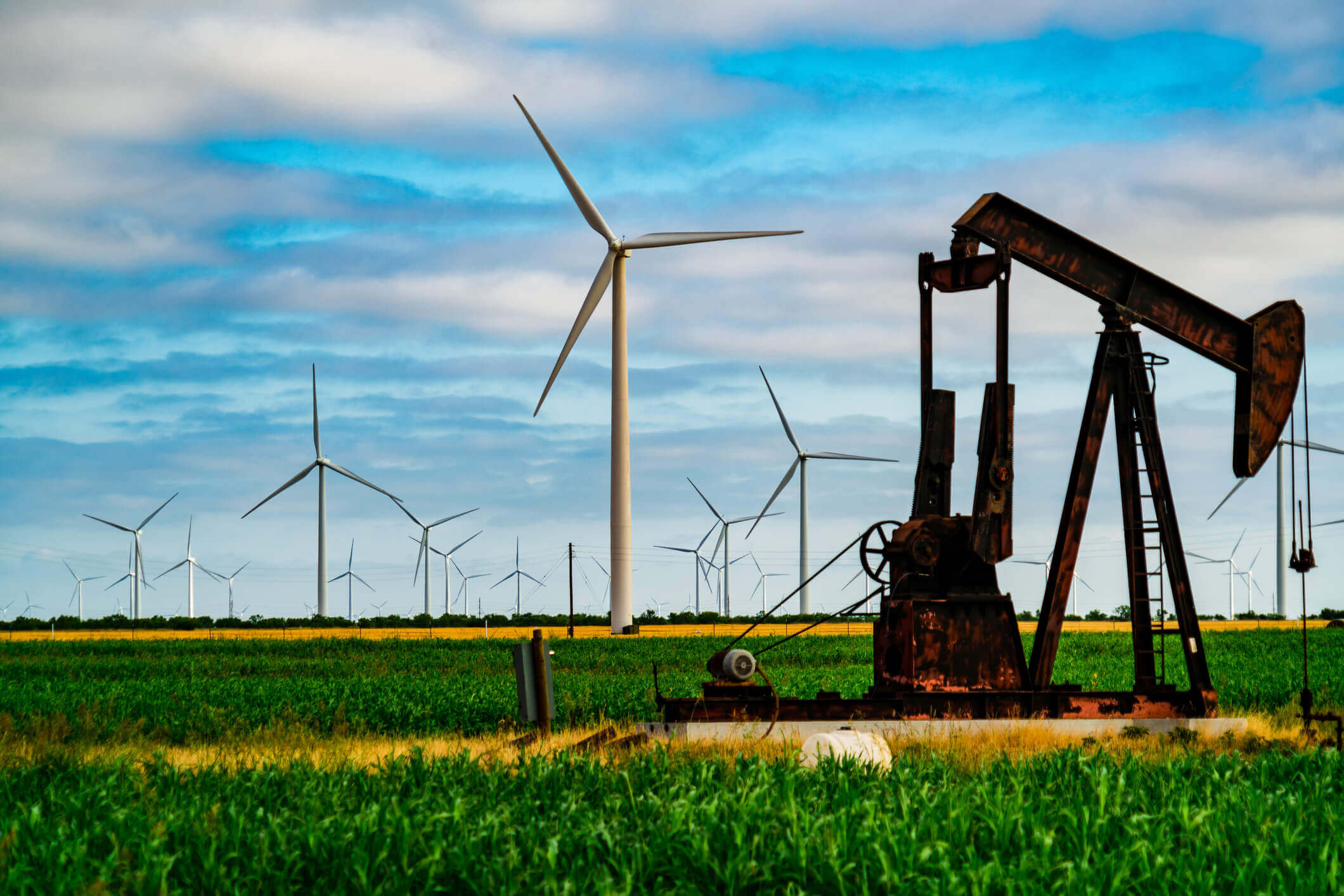 Old oil pump in front of big wind turbines on a Texas plain