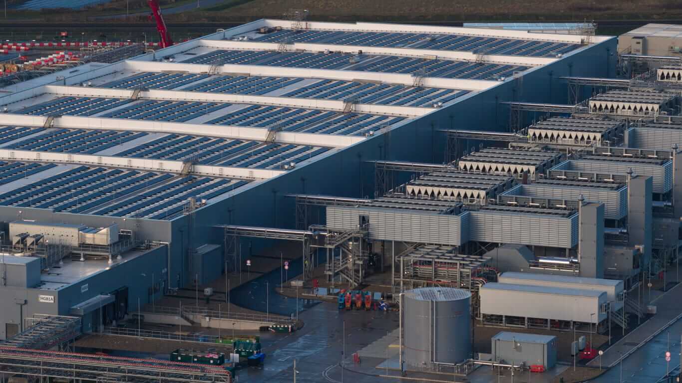 Aerial drone video of a large data center building exterior, representing the massive technological infrastructure required for storing, processing data, and delivering global digital services.